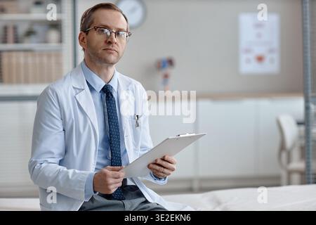 Porträt eines kaukasischen Mannes mittleren Alters, der Clipboard sitzend hält Stockfoto