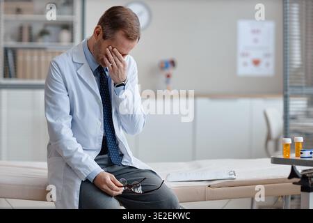 Kaukasischer Mann mittleren Alters Arzt sitzt allein und sieht in der Klinik gestresst aus Stockfoto