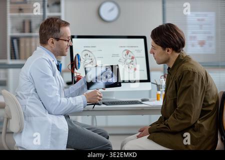 Kaukasischer Urologe mittleren Alters zeigt Ultraschallergebnisse für jungen erwachsenen Mann Stockfoto