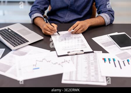 Ein Nahfoto der Arme eines jungen Mannes, der an einem Schreibtisch sitzt und mit Dokumenten arbeitet. Stockfoto