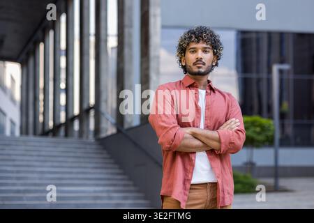 Porträt eines jungen Indianers in einem roten Hemd, Arme auf der Brust überkreuzt, ernsthaft in die Kamera schaut. Stockfoto