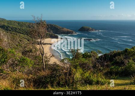 Ein ruhiger Blick auf einen Sandstrand, türkisfarbene Wellen und felsige Landzungen entlang der Küste von NSW. Stockfoto
