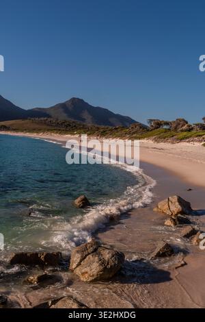 Sonnendurchflutete Bucht mit klarem Wasser, Felsen und Sandküste unter einem blauen Himmel in Tasmanien. Stockfoto