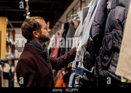 Bärtiger Mann, der Wintermantel im Bekleidungsgeschäft wählt Stockfoto