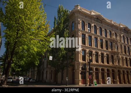 Historisches mehrstöckiges Gebäude mit Bogenfenstern und kunstvollen Details, umgeben von grünen Bäumen im Skidmore Old Town District, Portland, Oregon Stockfoto