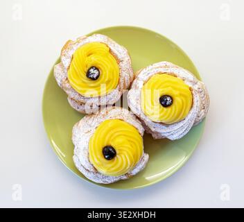 Neapolitanische Choux-Creme-Puffs, bekannt als Zeppole di San Giuseppe, sind traditionelle italienische Desserts mit süßem Pudding und dunklen Wildkirschen, die mit Puderzucker bestäubt sind Stockfoto