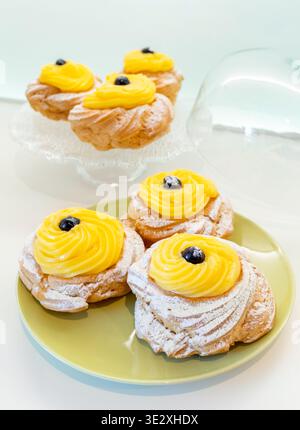 Zeppole di San Giuseppe, traditionelles italienisches Choux-Gebäck mit weichem Ring, einem Wirbel reichhaltiger Puddingcreme und einer dunklen schwarzen Kirsche auf der Oberseite, die mit Puderzucker bestäubt ist Stockfoto