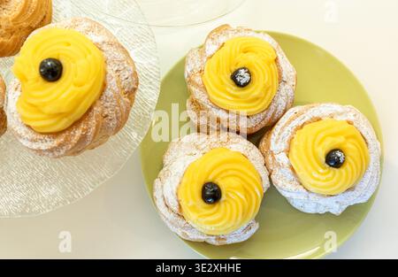 Traditionelles italienisches Zeppole di San Giuseppe Gebäck mit Choux-Teig, gelber Gebäckcreme, wilden schwarzen Kirschen und Puderzucker, das die italienische kulinarische Tradition symbolisiert Stockfoto