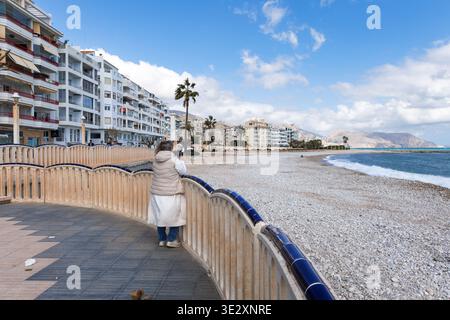 Blick auf die Promenade von Altea mit einem Touristen mit Blick auf den Kiesstrand und das Mittelmeer in Altea am 19. März 2026, Spanien Stockfoto