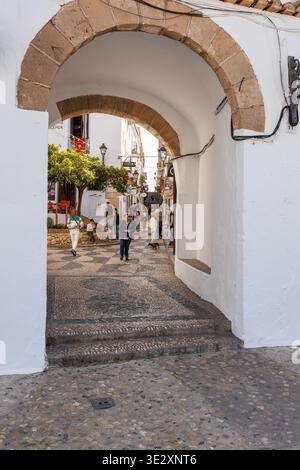 Blick durch einen Steinbogen in Richtung einer geschäftigen Altstadtstraße in Altea am 19. März 2026, Spanien Stockfoto