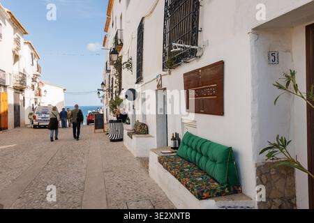 Touristen, die am 19. März 2026 an einem Weinladen in einer typischen Straße von Altea vorbeilaufen, Spanien Stockfoto