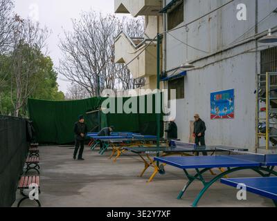 Wuhan, China - 4. März 2025: Menschen spielen Tischtennis an blauen Tischtennistischen im Freien in einem Wohngebiet. Das Bild zeigt die öffentliche Fitness-Facil Stockfoto