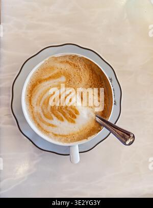 Eine Tasse Cappucino-Kaffee mit Blattdesign im Schaum wird auf einer Marmorarbeitsfläche in einem Café in Porto, Portugal, serviert. Stockfoto