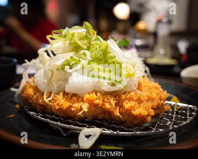 Knuspriges paniertes Schweinekotelett mit erfrischendem geriebenem Rettich und in Scheiben geschnittenen Zwiebeln auf einer dunklen Keramikplatte. Stockfoto
