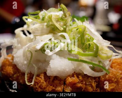 Knuspriges paniertes Schweinekotelett mit erfrischendem geriebenem Rettich und in Scheiben geschnittenen Zwiebeln auf einer dunklen Keramikplatte. Stockfoto