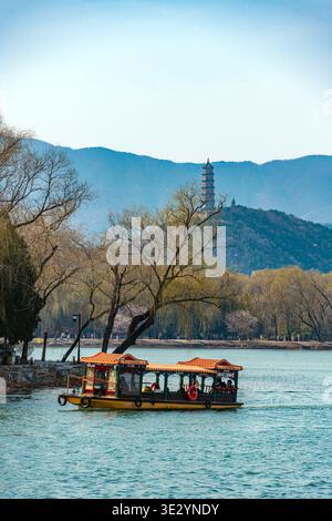 Peking, China - 19. März 2026: Touristen auf einem traditionellen Boot überqueren den Kunming-See im Sommerpalast mit westlichen Hügeln und Pagode. Stockfoto
