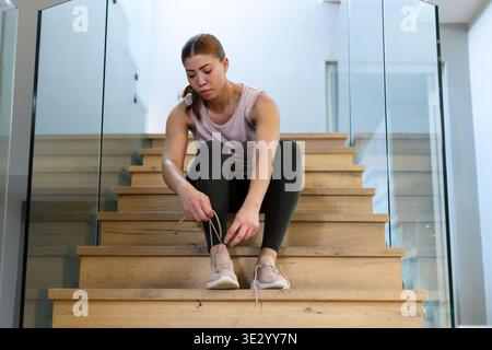 Afroamerikanerin sitzt auf Treppen und bindet leichte Schuhe in der Nähe von Glasgeländern und trägt Panzerleggings Stockfoto