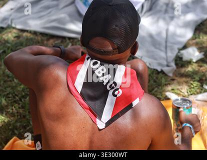 Ein Maskerader von hinten mit einer schwarzen Mesh-Baseballmütze und einem rot-weißen und schwarzen Bandana mit dem „TOBAGO“. Stockfoto