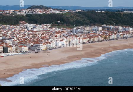 Panoramablick auf den Sandstrand und die Küstenstadt Nazare Portugal mit roten Dachgebäuden entlang der Küste und Rolling Atlant Stockfoto