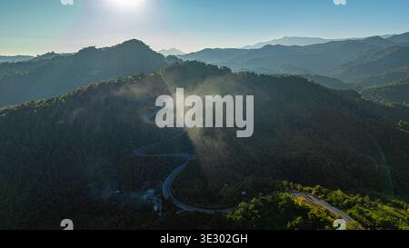 Drohnenblick auf eine malerische Serpentinenstraße, die sich durch dichte tropische Berge in der Provinz Nan schlängelt. Die Kombination aus Nebel, Grün und dramatischen Kurven Stockfoto