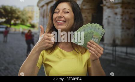 Die Frau im Mittelalter zeigt chilenische Peso-Banknoten mit Daumen nach oben beim Bau am kolosseum; Vertrauen in die Tourismusfinanzierung. Stockfoto