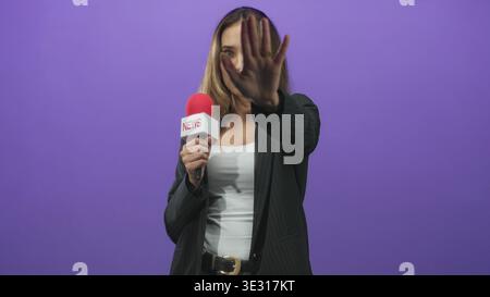 Reporterin mit Mikrofon mit rotem Schaum, Handfläche zur Kamera im Studio hochgehoben; Trotz-Grenze. Stockfoto
