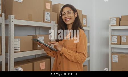 Frau, die Tablets überprüft, während sie Paketetiketten an Metallregalen im Gebäude anzapft; Effizienz fokussiert die Produktivität. Stockfoto