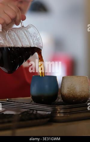 Karachi, Pakistan - 20. März 2026: Nahaufnahme einer Person, die frisch gebrühten Kaffee aus einer Glaskaraffe in eine Keramikschale gießt Stockfoto