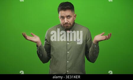 Der Mann zuckt mit den Schultern mit den Handflächen nach oben und geschlossenen Augen auf dem grünen Bildschirm des Studios, ein olivfarbenes Hemd sichtbar; Zweifel an Verwirrung. Stockfoto