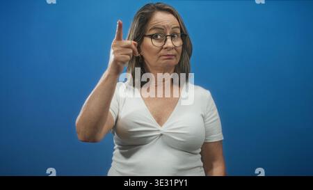 Hispanische Seniorin mit grauem Haar und Brille, die weiße Spitze trägt, Finger zum Tempel im Studio; nachdenkliche Reflexion. Stockfoto