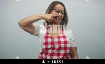 Eine ältere Frau mit roter Karomuster und Brille zeigt mit dem Finger an die Nase und lächelt direkt in die Kamera im Studio; warme Hausmannskost. Stockfoto