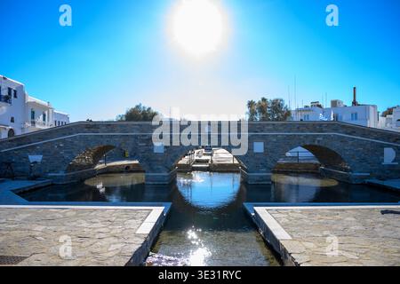Steinbrücke mit drei Bögen über einen Kanal in Mykonos, Griechenland, mit weiß getünchten Gebäuden und klarem blauem Himmel Stockfoto