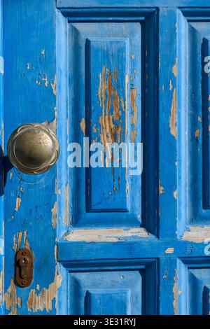 Verwitterte, blau lackierte Holztür mit abblätternder Farbe, Messing-Türknauf und Schlüsselloch, mit altertümlicher Patina und versehrter Oberfläche Stockfoto