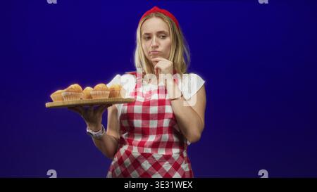 Die Chefin im Studio hält hölzerne Muffins mit Hand und Finger bis Kinn, um Gebäck zu untersuchen; Nachsicht. Stockfoto