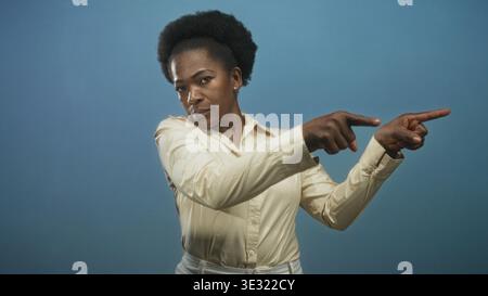 Frau mit beigefarbener Bluse zeigt beide Zeigefinger nach außen, während sie im Studio zur Kamera geneigt ist; Vertrauensanweisungen. Stockfoto