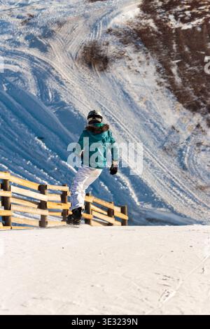 Ein Wintersportler genießt einen sonnigen Tag auf einem schneebedeckten Berghang neben einem rustikalen Holzzaun mit Skipisten im Hinterland Stockfoto
