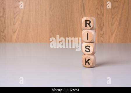 Vertikaler Stapel aus Holzblöcken, in denen das Wort RISIKO in Großbuchstaben geschrieben wird, auf einem grauen Schreibtisch mit natürlichem Holzhintergrund. Konzeptionelles Bild für Finanzen Stockfoto