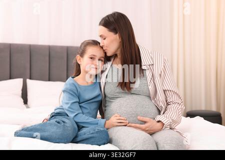 Schwangere Frau und ihre Tochter sitzen zu Hause auf dem Bett Stockfoto