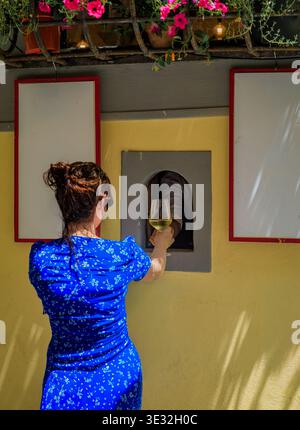 Eine Frau in blauem Kleid kauft ein Glas Weißwein aus einer historischen Buchetta del vino Weinfenster im Centro Storico, Florenz, Toskana, Italien Stockfoto