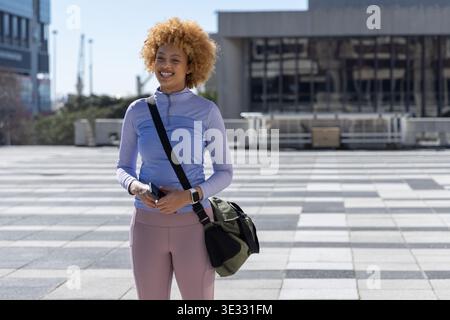 Afroamerikanische Frau, die auf dem gemusterten plaza in sportlicher Kleidung steht und Smartphone und Seeschiffle hält Stockfoto