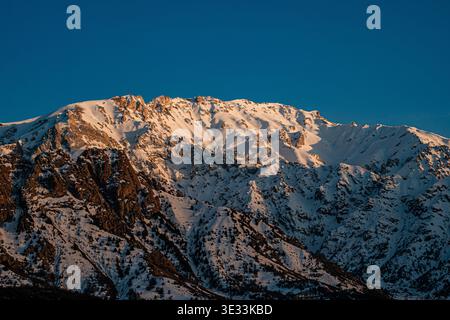 Ein atemberaubender Blick auf einen schneebedeckten Berggipfel, der von Sonnenlicht vor einem klaren blauen Himmel beleuchtet wird und die Schönheit der Winterlandschaft zeigt. Stockfoto