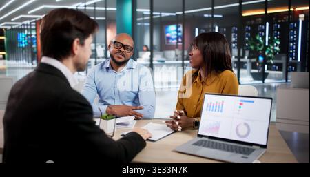 Finanzberater erklärt Einem jungen Paar, das ein Notebook verwendet, Investitionspläne. Der Buchhalter Erörtert Steuerstrategien Stockfoto