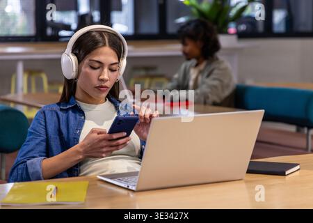Verschiedene Studenten studieren in der Bibliothek, Frauen mit Kopfhörern über Smartphone mit Laptop, Notebook Stockfoto