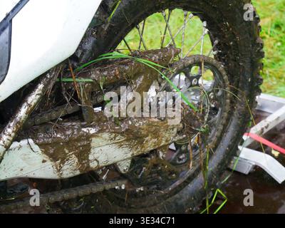 Schlammiges Hinterrad des Motocross-Bikes, bedeckt mit Schmutz und Gras. Extreme Enduro-Motorraddetails nach Off-Road-Wettkämpfen. Verschmutztes Zahnrad und Kette von c Stockfoto