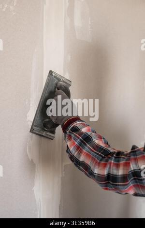 Bauarbeiter, der Schleifpapier zum Glätten der Wandoberfläche verwendet, während der Hausrenovierung fertig stellen. Nahaufnahme Stockfoto
