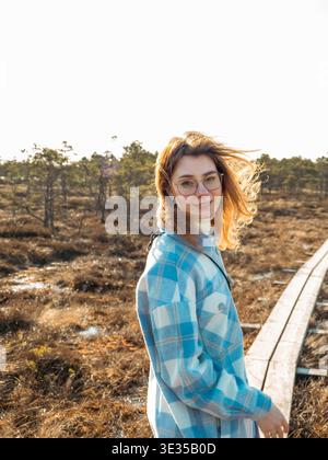 Junge Frau in karierter Jacke lächelt auf der Kakerdaja Moorpromenade im Frühling Estland Stockfoto