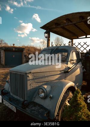 Alter weißer GAZ-Truck aus der Sowjetzeit unter hölzerner Pavillon mit Straßenlaterne in Estland, Frühling Stockfoto