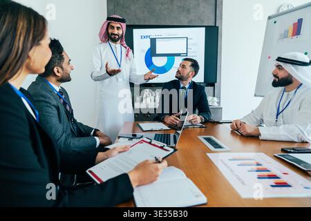 Team-Meeting in einem modernen Büro in dubai, arabischer Geschäftsmann, der eine Präsentation mit Daten und Diagrammen anführt, während die Kollegen zusammenarbeiten Stockfoto