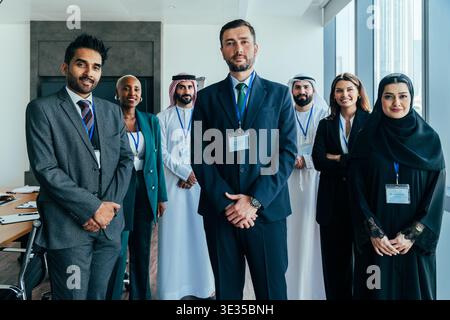Ein multiethnisches Unternehmensteam lächelt und steht zusammen in einem modernen Büro in dubai, zuversichtliche Profis in formeller Kleidung, die die globale Zusammenarbeit demonstrieren Stockfoto