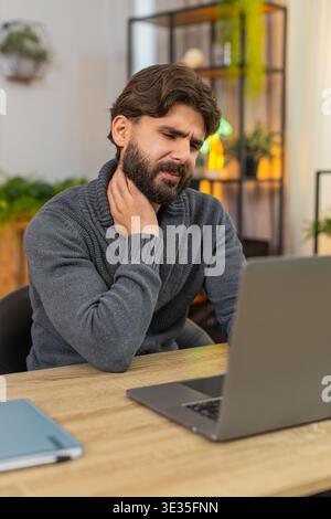 Indischer Mann zu Hause arbeitet am Laptop fühlt Nackenschmerzen reiben Nackenrunzeln stoppt Aufgabe zu ruhen schließt den Deckel. Ein Araber an der Rezeption massiert den Nacken langsamer Atem. Unglückliche Stimmung braucht Pause nach Anstrengung von langer Sitzung Stockfoto